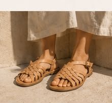 Detalle de una modelo con sandalias de piel sobre piedra clara